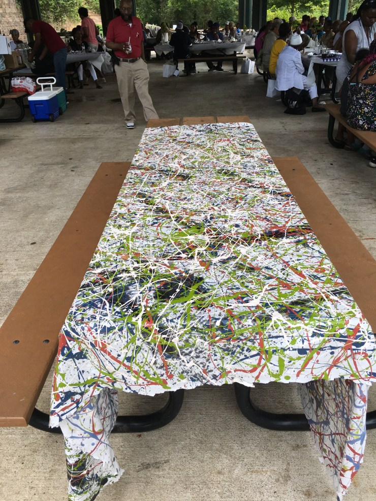 Drip painting on a picnic table with people in the background.