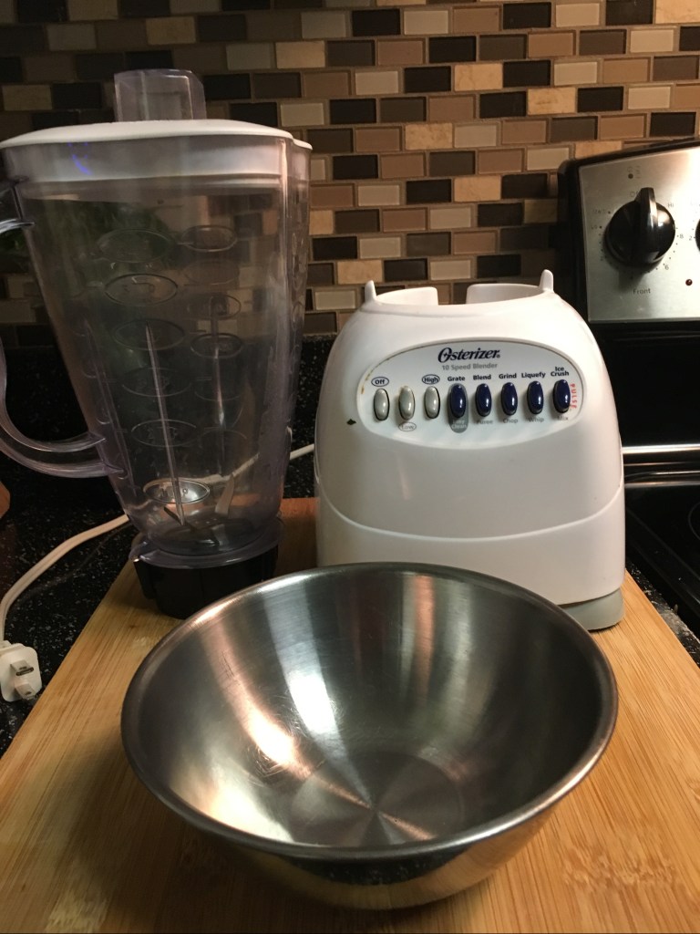 A blender behind a small stainless steel bowl.