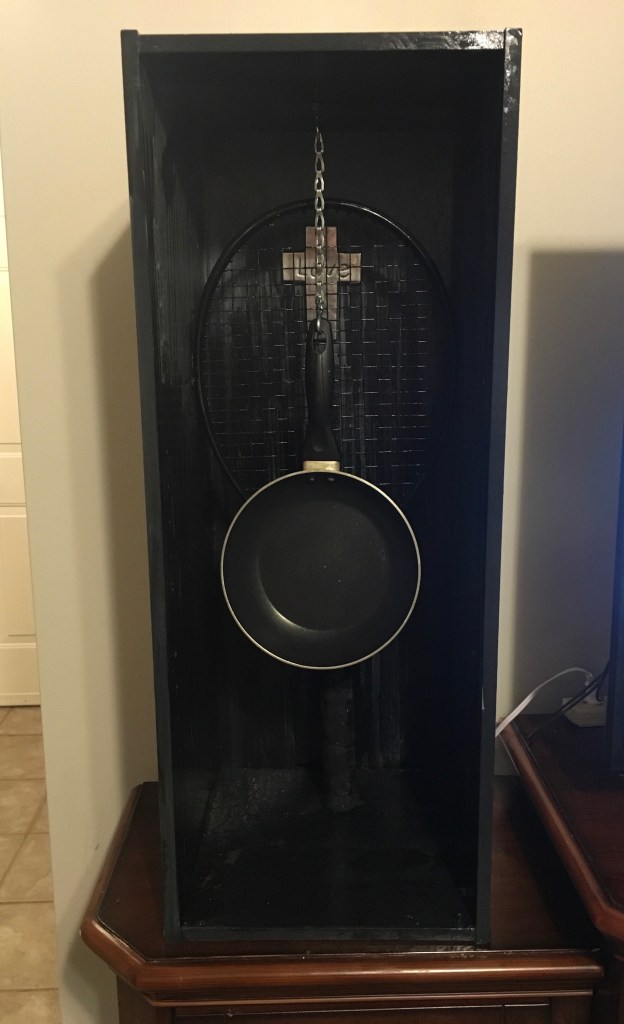 Black cabinet with cross, tennis racket and frying pan.