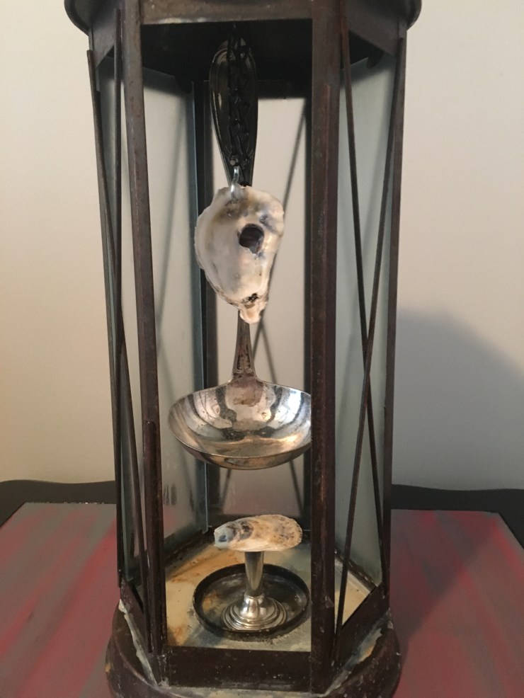 Sculpture of silver ladle and oyster shells inside lantern.