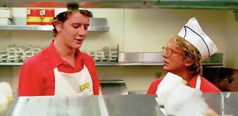 Two fast food employees discussing burger composition.