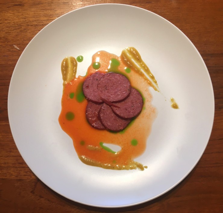 Salami on a plate with yellow, red and green sauces.