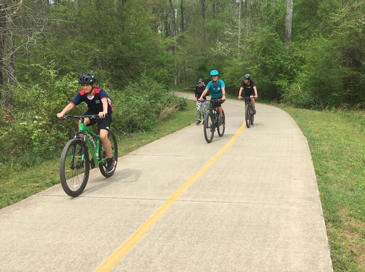Three cyclists passing a jogger on a path.