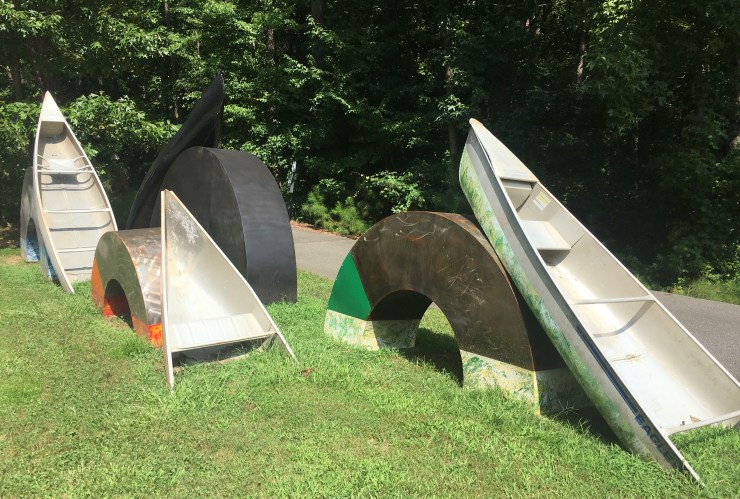 Statue of canoes leaning on tractor tires.