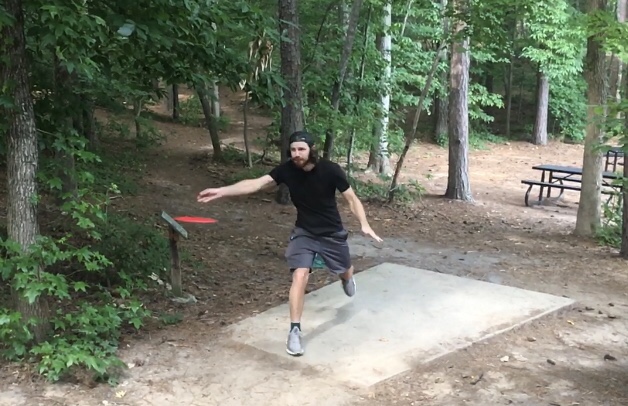Man flinging a red disc golf frisbee.