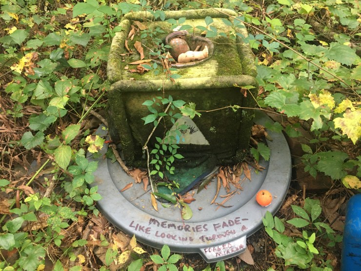 Plants over growing a laundry hamper with a doll head in the middle.