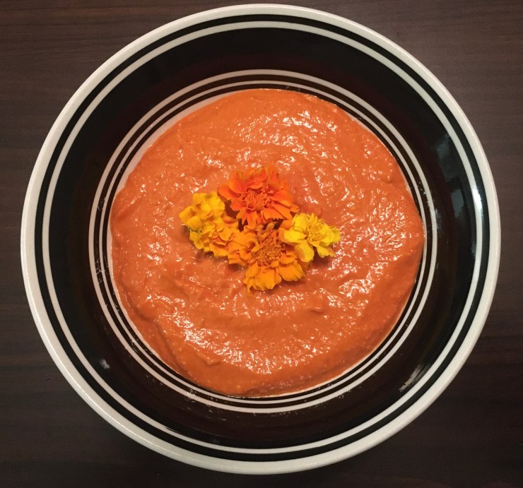 Romesco sauce with orange and yellow flowers in a black and white bowl.