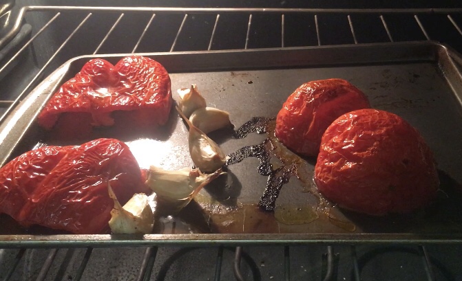 Red bell peppers, garlic and tomatoes roaring in an oven.