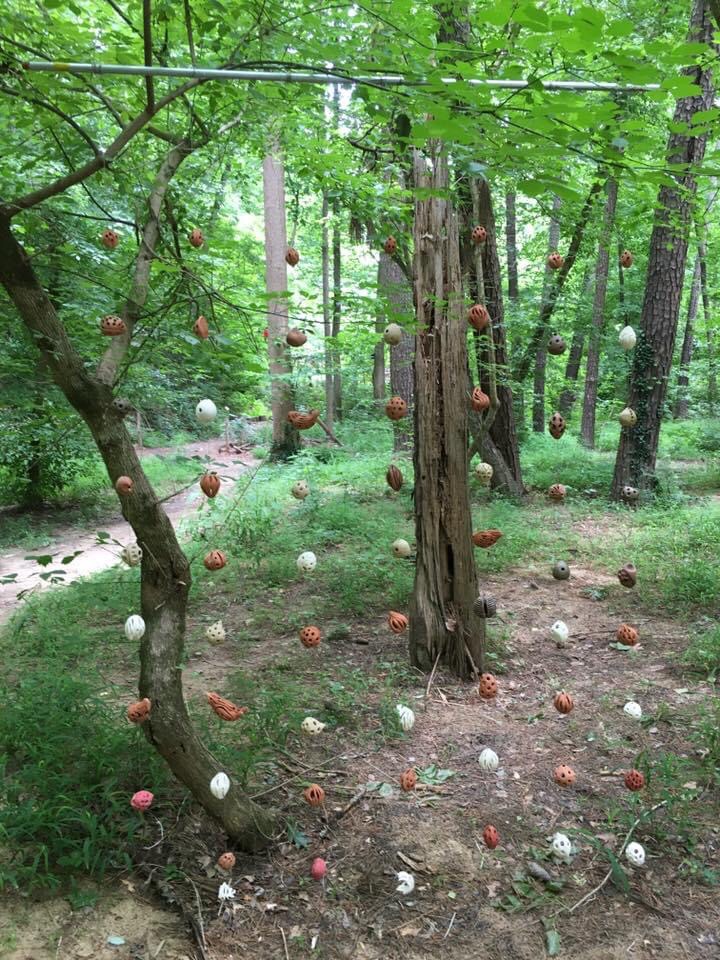 Easter egg-like art hanging in a forest.
