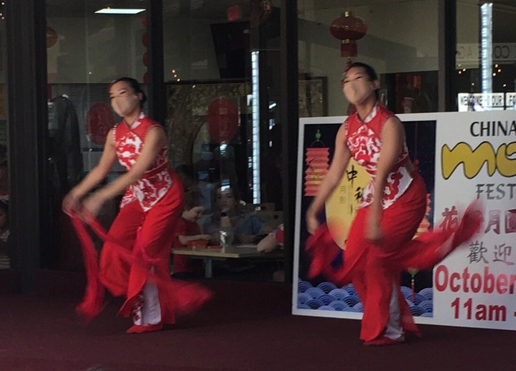 Two women in traditional Chinese costumes twirling red ribbons.