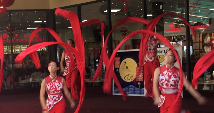 Four women in traditional Chinese costumes twirling red ribbons.