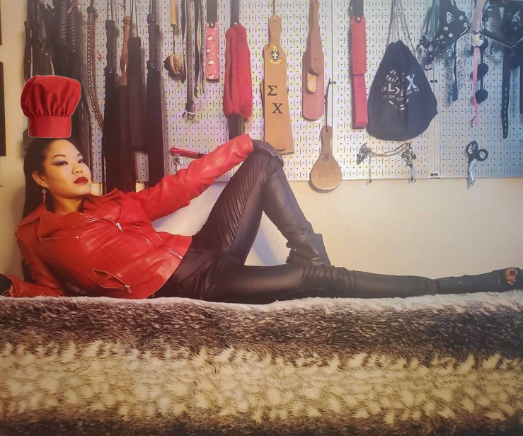 Dominatrix laying on a table wearing a red chef's hat.