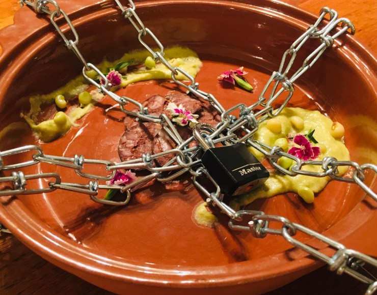 Blood sausage and zipper pea puree locked with chains in a terra cotta plate.
