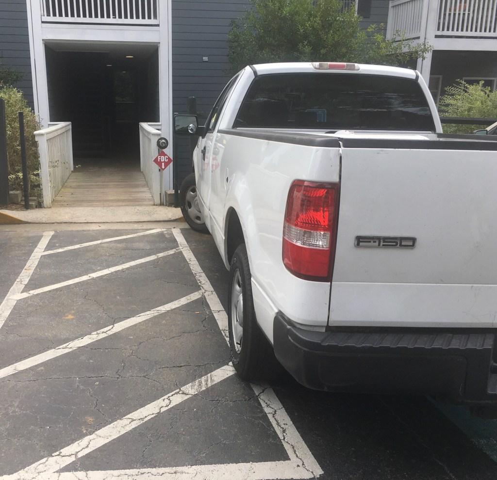 White truck parked over the assigned lines of a handicapped parking space.