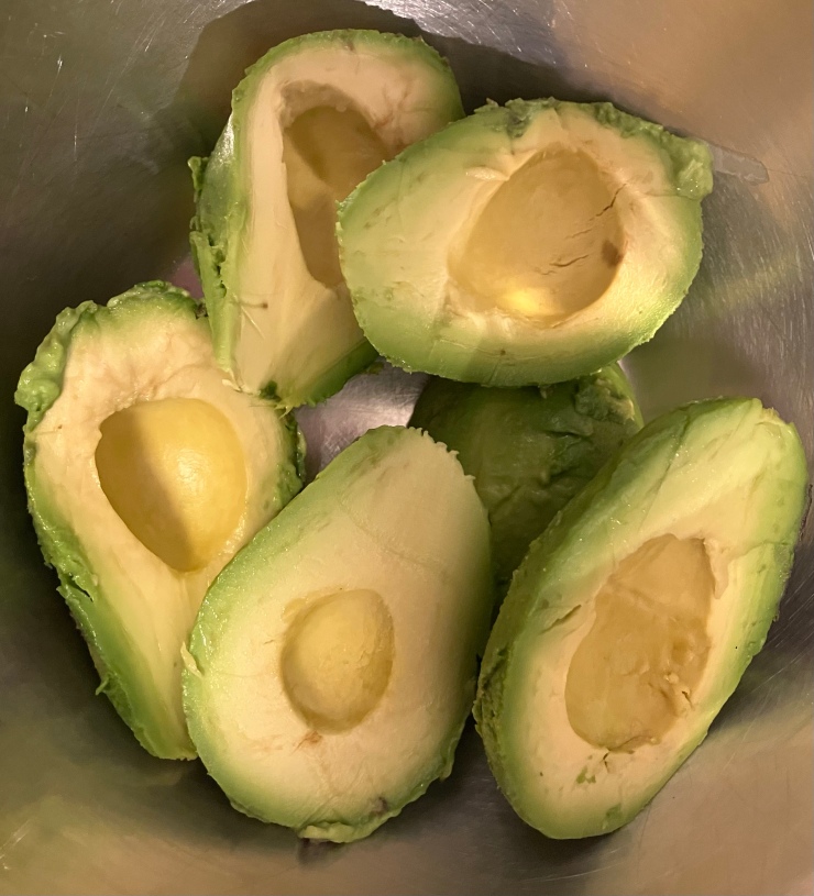 Six avocado halves in a mixing bowl.