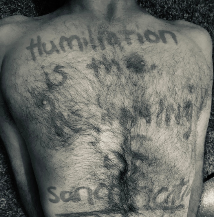 Black and white photo of a shirtless torso with words scribbled in lipstick on the chest.
