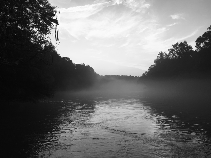 Black and white photo of fog drifting over a river.